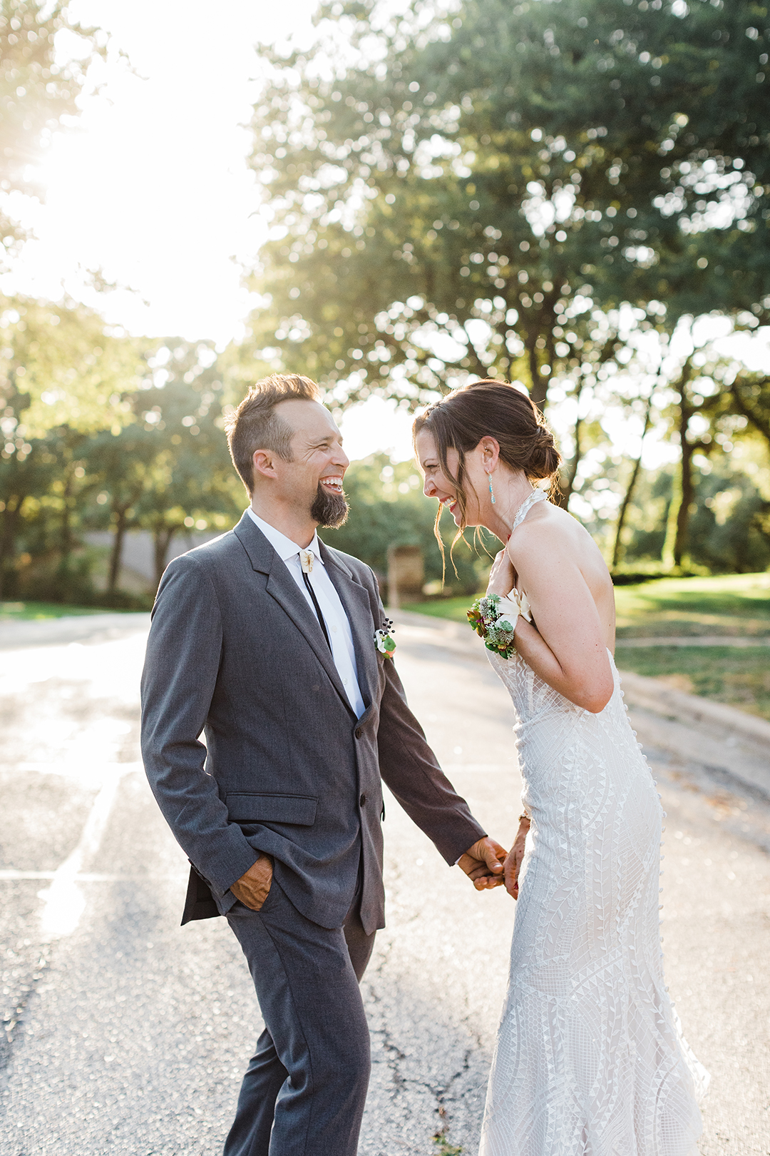 groom on left side and bride on right side holding hands, laughing together, with golden hour sunlight behind them